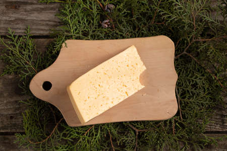 a piece of hard cheese lies on a wooden board in the branches with a Christmas tree, table decor