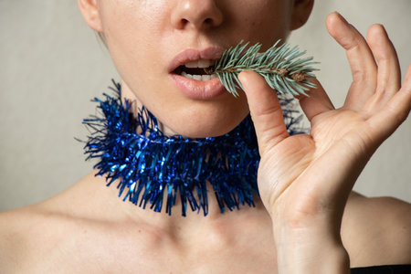 blue Christmas garland on the girl's neck and a spruce branch in her mouth, waiting for the new...