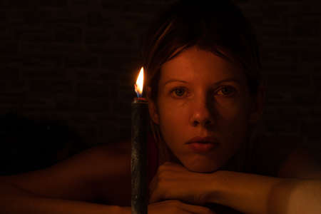 the girl's face in the dark against the background of a black burning candleの写真素材