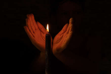 hand in the dark near the flame of a black candle close up