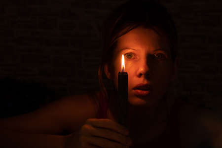 the girl's face in the dark against the background of a black burning candleの写真素材
