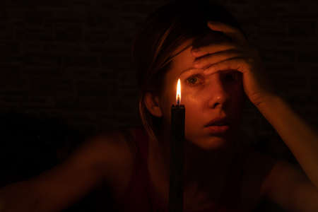 the girl's face in the dark against the background of a black burning candleの写真素材