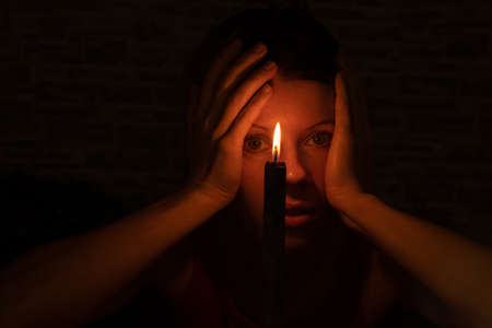 the girl's face in the dark against the background of a black burning candleの写真素材
