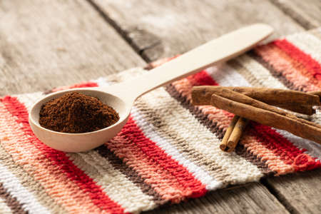 wooden spoon with ground coffee and cinnamon sticks on a wooden table lie on a striped multi-colored...