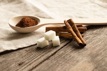 wooden spoon with ground coffee and cinnamon sticks and sugar cubes on a wooden table in the sunlightの写真素材