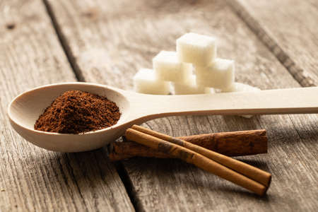wooden spoon with ground coffee and cinnamon sticks and sugar cubes on a wooden table in the sunlightの写真素材