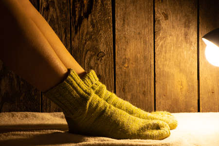 female feet in knitted socks on the floor next to a teddy bear poured the lamp on at nightの写真素材