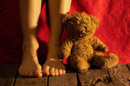 female feet on the floor next to a teddy bear in the dark with a night lampの写真素材