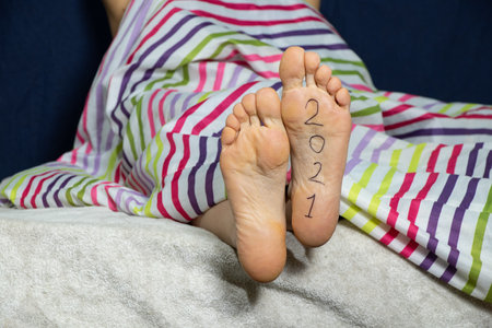 2021 written on the female foot of a girl lying on the bed at home in the bedroomの写真素材