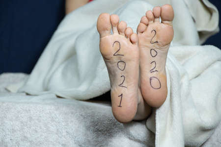 2021 and 2021 is written on the female feet of a girl lying on a bed at home in a bedroomの写真素材