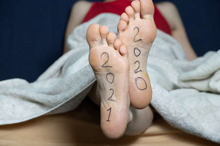 2021 and 2021 is written on the female feet of a girl lying on a bed at home in a bedroomの写真素材