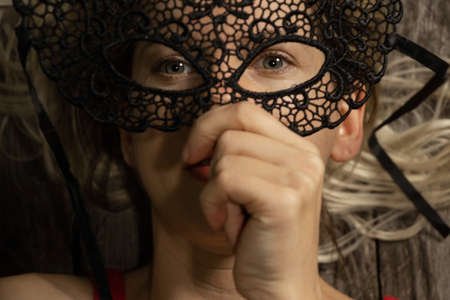 girl holding a black carnival mask in front of her faceの写真素材