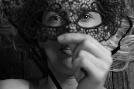 girl holding a black carnival mask in front of her faceの写真素材