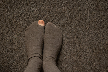 a woman's toe came out of a torn sock on the floor of the house close-up, female feet on the floorの写真素材