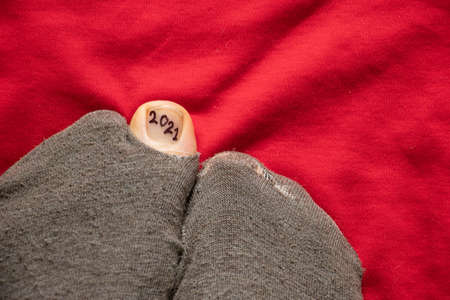 2021 is written on the toe nail sticking out of a torn sock on the floor, new year in povertyの写真素材