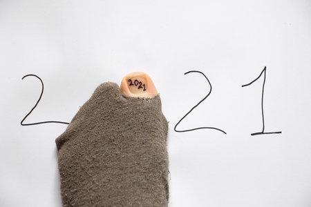 2021 is written on a white background and instead of zero there is a foot in a sock with a hole from which a finger sticks out, poverty in 2021の写真素材