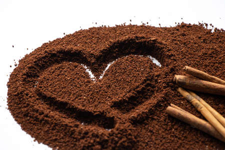 ground coffee scattered on a white background a heart is drawn on it and two cinnamon sticks lie next to itの写真素材