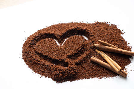 ground coffee scattered on a white background a heart is drawn on it and two cinnamon sticks lie next to itの写真素材