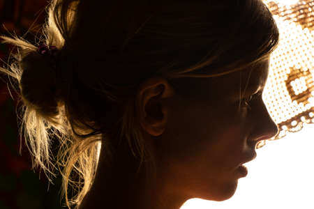 portrait of a young girl in a dark room against the background of a bright lampの写真素材