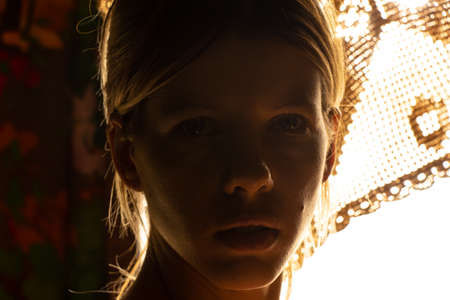 portrait of a young girl in a dark room against the background of a bright lampの写真素材