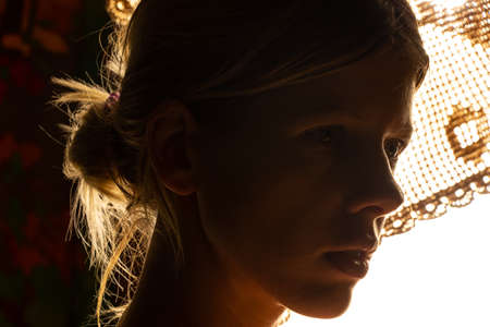 portrait of a young girl in a dark room against the background of a bright lampの写真素材