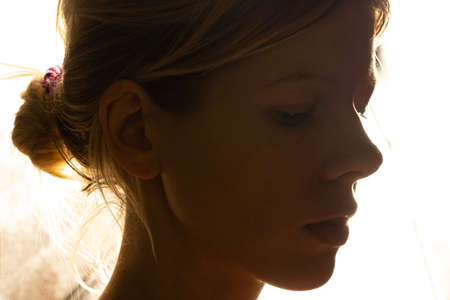 portrait of a young girl in a dark room against the background of a bright lampの写真素材