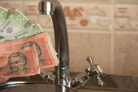 a woman's hand holds a Ukrainian 10 20 hryvnia near the kitchen tap, water pricesの写真素材