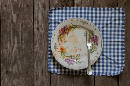 a dirty plate lies on a blue napkin in a cage on a wooden table in the kitchen after lunchの写真素材