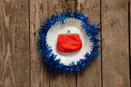 red wallet lies on a white plate decorated New Year's colored ribbon on a wooden background...