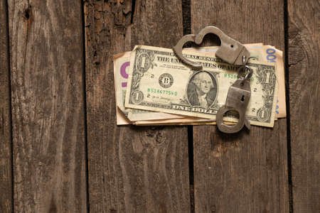 american dollars lie on an old wooden table next to handcuffs, finances and corruptionの写真素材