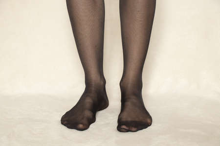 female legs in black nylon tights on a white carpet at home