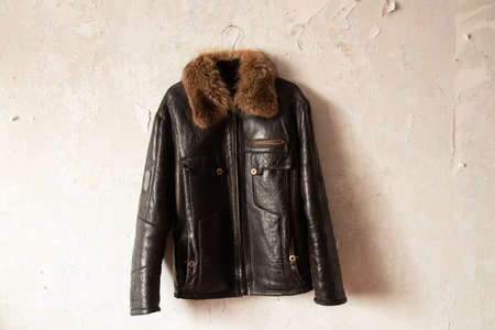 black leather winter men's jacket hanging on a hanger on the wall indoorsの写真素材