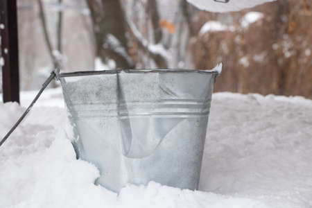an iron gray bucket stands in the snow on wells in winter in Ukraineの写真素材