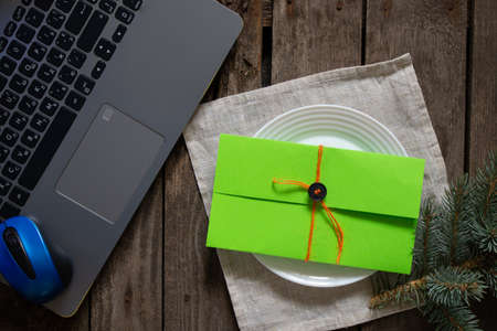 green gift envelope lies on the table near the laptop and a pine branch, a gift for the new yearの写真素材