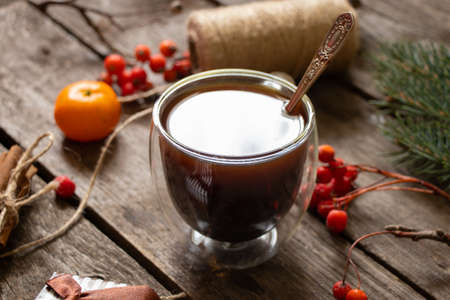 cup with coffee next to a branch of a christmas tree tangerine cinnamon on a wooden table, christmas table with coffee in the morningの写真素材