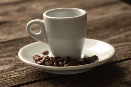 one white cups and a saucer with grains of coffee stand on a wooden table in the morning in the kitchenの写真素材