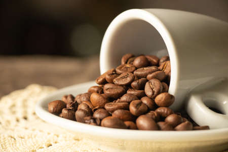 one white cups and a saucer with grains of coffee stand on a wooden table in the morning in the...