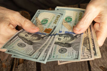 hands of an old woman on american dollars on a wooden table close upの写真素材