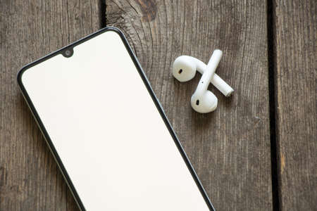 phone with white screen wireless headphones on wooden table, technologyの写真素材