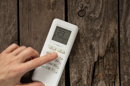 female hand switches button on white air conditioner remote control on wooden backgroundの写真素材