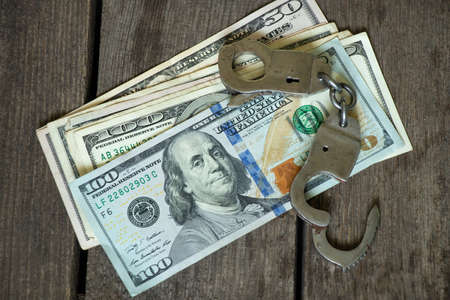 american dollars and handcuffs on a wooden table, financial crimes