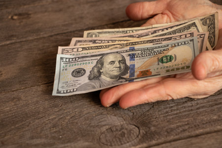 hands of an old woman on american dollars on a wooden table close upの写真素材