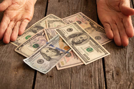 hands of an old woman on american dollars on a wooden table close up