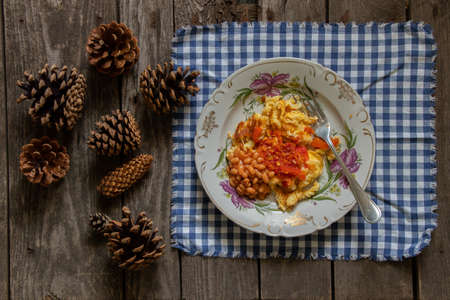 fried egg with beans in a tomato in a plate on a wooden table on a tablecloth, breakfast