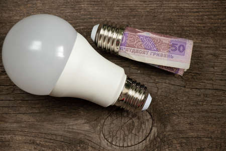 lamp holder with a fifty hryvnia bill screwed into it in the hands of a woman on a wooden background, the price of electricityの写真素材