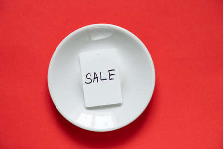 white price tag with the inscription discount lies on a white plate on an isolated red backgroundの写真素材