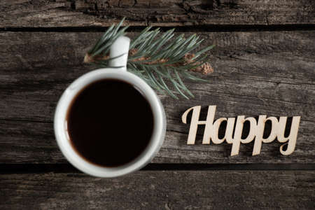 a cup of coffee and a neighboring pine branch and next to the word in english happy on a wooden...