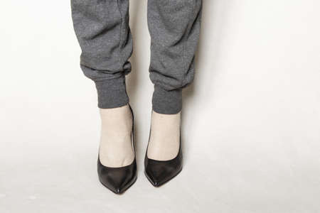 a young girl in gray sweatpants and black pointed toe high-heeled shoes stands on a white carpet at homeの写真素材