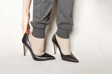 a young girl in gray sweatpants and black pointed toe high-heeled shoes stands on a white carpet at homeの写真素材