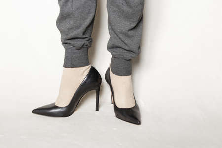 a young girl in gray sweatpants and black pointed toe high-heeled shoes stands on a white carpet at homeの写真素材